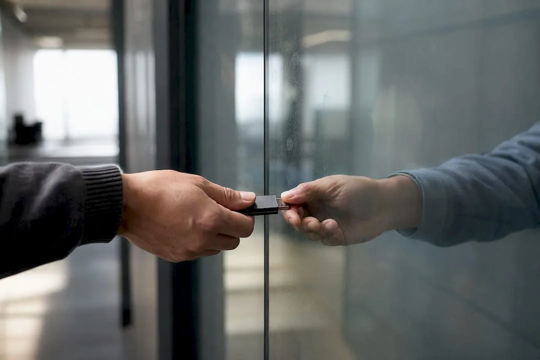 Two hands exchange a secure token through a protective glass.